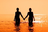 Couple walking into the sea at sunset.