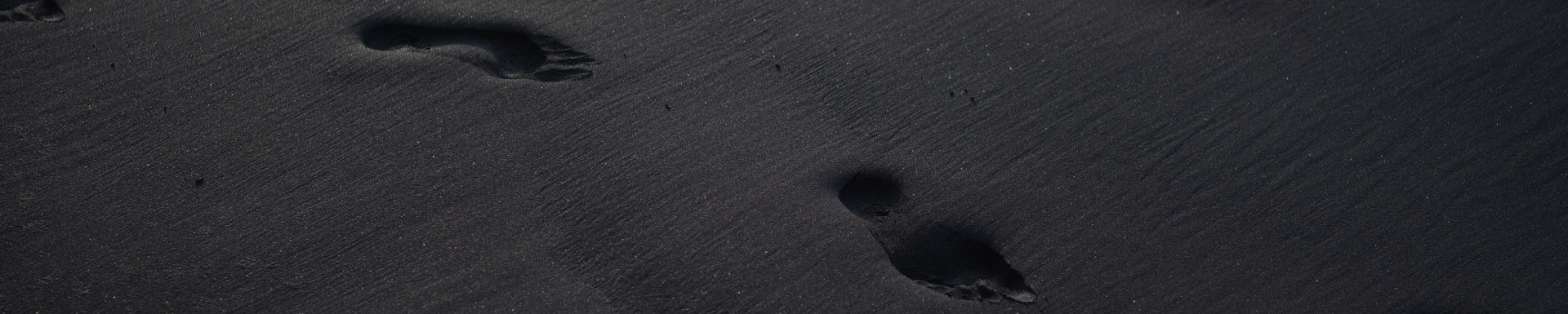 Fußspuren in schwarzem Strand