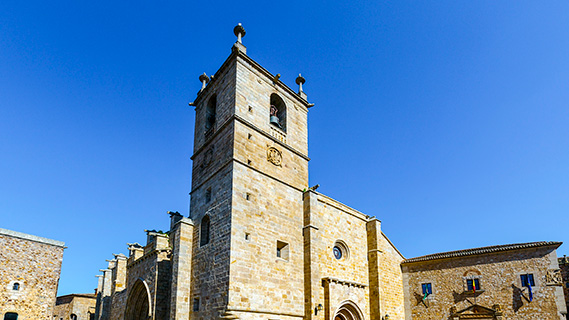 Ein imposanter Turm aus goldenen Steinblöcken mit Glockenturm und einem Portikus mit gotischen Bögen dominiert die Fassade der Konkathedrale