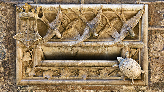 Aus der Mauer ragt ein steinerner Briefkasten hervor, der mit fünf fliegenden Schwalben verziert und von Efeublättern umrahmt ist