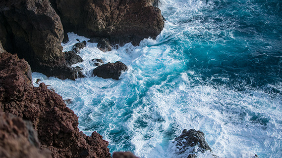 Das tiefblaue Wasser des Atlantiks bricht sich an dunklem, porösem Vulkangestein.