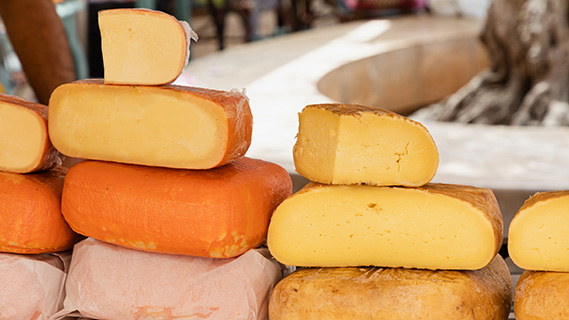 Auf der Theke eines Marktstands stapeln sich dicke Stücke und ganze Laibe gereifter Käse