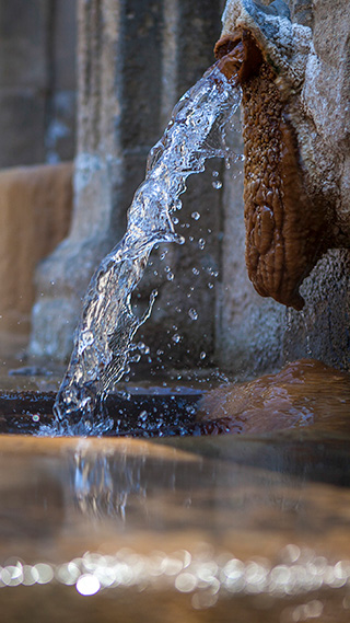 Aus einem alten Steinbrunnen sprudelt ein stetiger Strahl kristallklaren Wassers