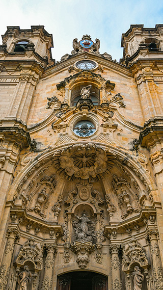 Die reich verzierte barocke Fassade aus ockerfarbenem Stein erhebt sich imposant und beherbergt in einer zentralen Nische die Skulptur des Heiligen Sebastian