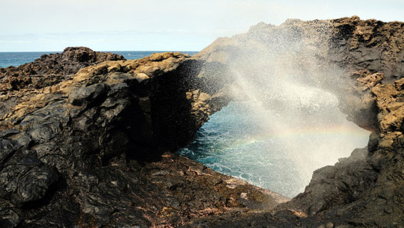 Ein heftiger Strahl Salzwasser schießt durch eine Öffnung im dunklen, schroffen Küstenfelsen in die Höhe