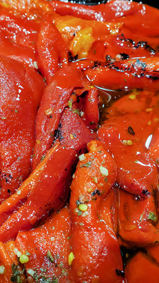 Mehrere geröstete, intensiv rote Piquillo-Paprikaschoten liegen in ihrem eigenen Saft und Öl