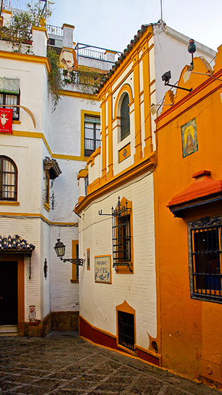 Eine schmale, gewundene Kopfsteinpflasterstraße wird von traditionellen andalusischen Fassaden eingerahmt