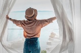 Turista abrindo as cortinas do seu quarto de hotel