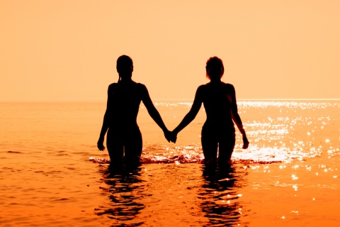 Casal entrando no mar durante o pôr do sol