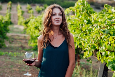 Una donna tra i vigneti con un calice di vino in mano