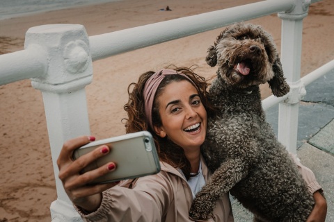  Tourist macht ein Selfie mit seinem Hund an einem Strand in Gijón, Asturien