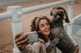 Turista che scatta un selfie con il proprio animale domestico in una spiaggia di Gijón, Asturie