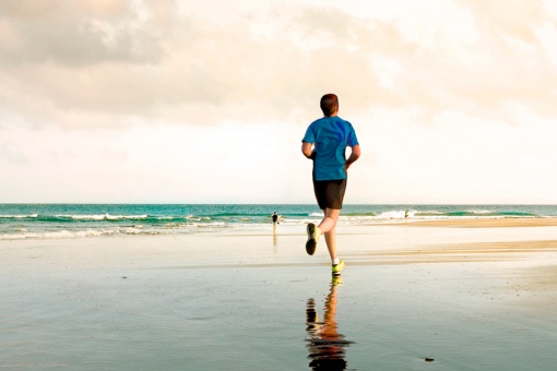Молодой человек бежит по пляжу Маспаломас в Гран-Канарии, Канарские острова