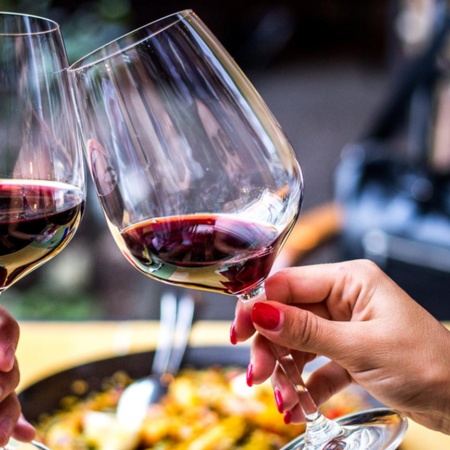 Brindis con vino tinto y paella de fondo