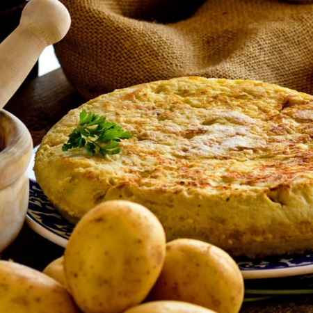 Tortilla ziemniaczana z produktami do jego przygotowania i moździerzem