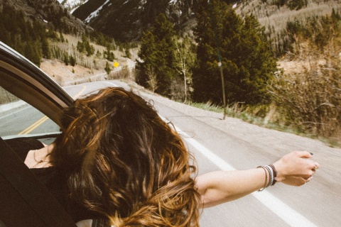  Chica se asoma por la ventanilla de un coche en una carretera de montaña