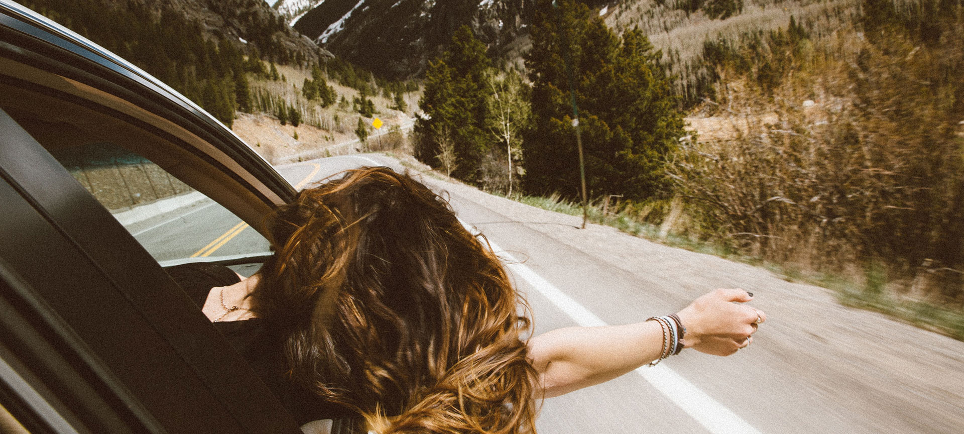 Chica se asoma por la ventanilla de un coche en una carretera de montaña  Chica se asoma por la ventanilla de un coche en una carretera de montaña