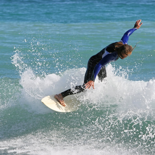 Surfista deslizando la tabla en la cresta de una ola en una playa de Almería, Andalucía