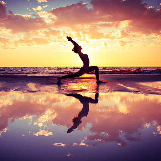 Une femme faisant du yoga sur la plage, au coucher du soleil