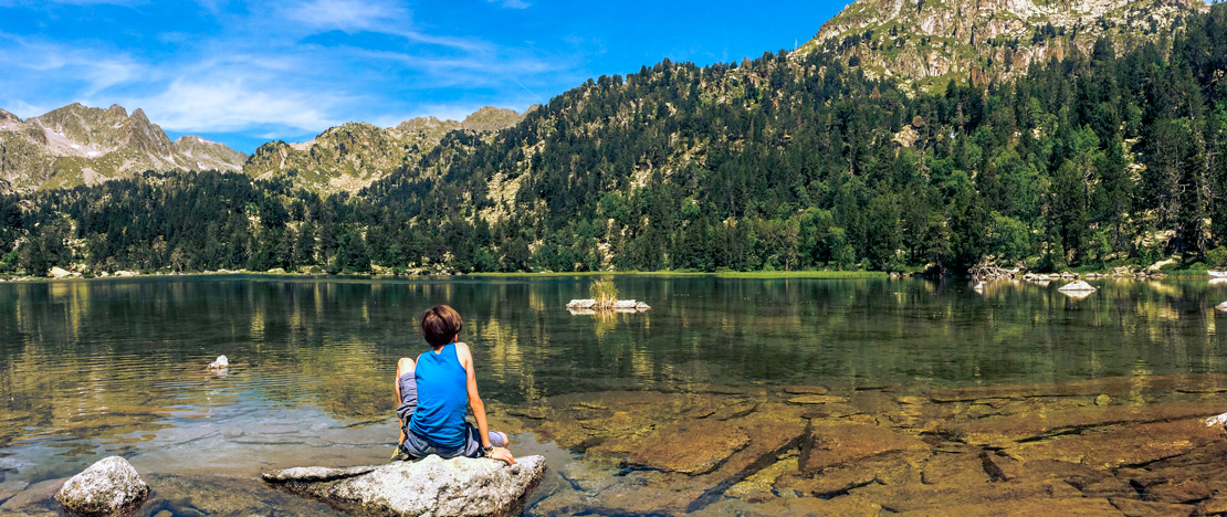 Enfant assis près d'un des lacs du parc national d'Aigüestortes i Estany de Sant Maurici à Lérida, en Catalogne Enfant assis près d'un des lacs du parc national d'Aigüestortes i Estany de Sant Maurici à Lérida, en Catalogne