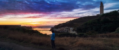 Junge Frau betrachtet den Sonnenuntergang beim Herkulesturm, Galicien