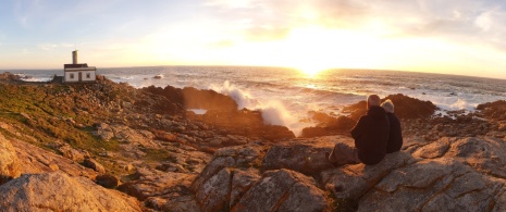 Turistas contemplando la puesta de sol en el faro de Corrubedo en A Coruña, Galicia