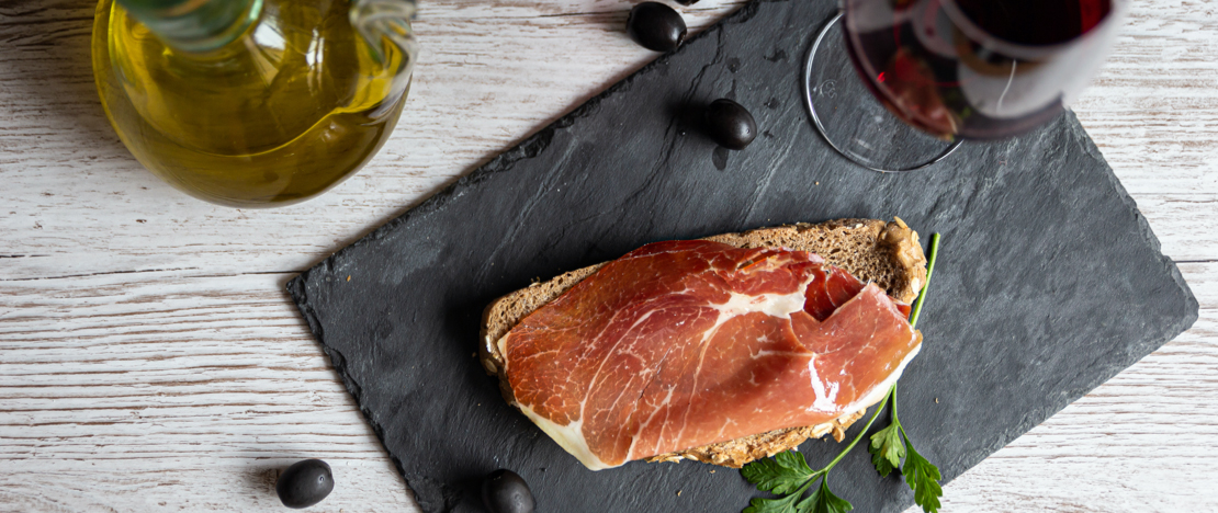 Detalle de tapa de jamón con aceite y copa de vino tinto