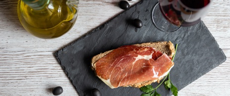 Detalhe de tapa de presunto com óleo e taça de vinho tinto 